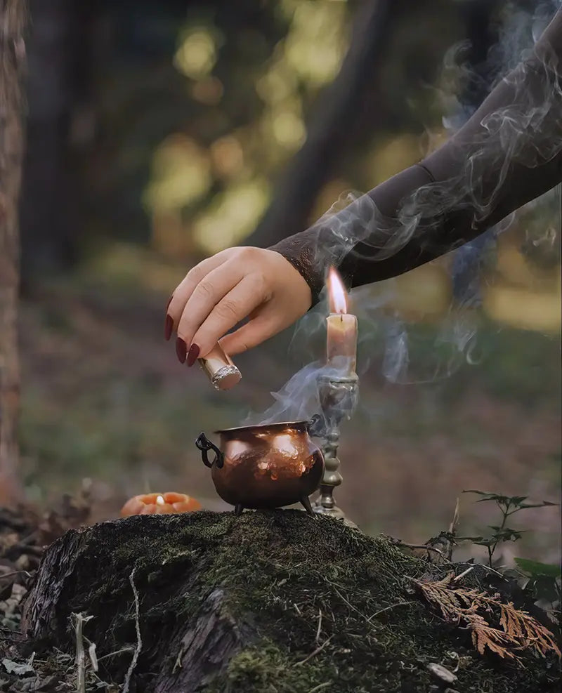 hand performing spell ritual with candle and cauldron outdoors